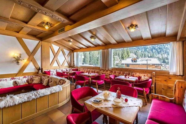 Uvnitř dřevem obložené restaurace s červenými židlemi a pohledem na zasněžené stromy.