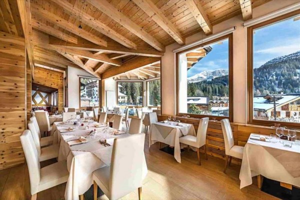 Restaurace s dřevěným interiérem a velkými okny s výhledem na zasněžené hory.