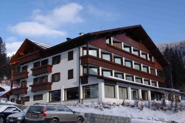 Horský hotel s dřevěnými balkony a sněhem pokrytou střechou.
