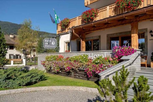 Vstup do hotelu Baita dei Pini s květinami na terase.