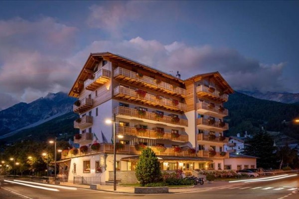 Vícepodlažní dřevěný hotel osvětlený pouličními lampami v horách za soumraku.