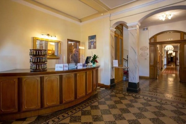 Hotelová recepce s dřevěným pultem a zaměstnancem v obleku.