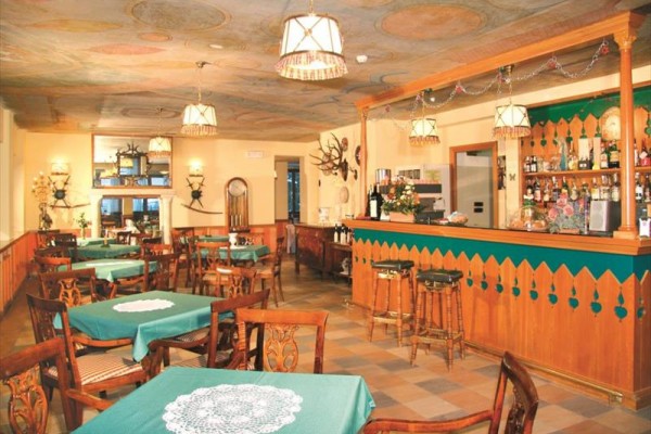 Rustikální interiér restaurace s dřevěnými stoly a sloupy, strop zdobený malbami.
