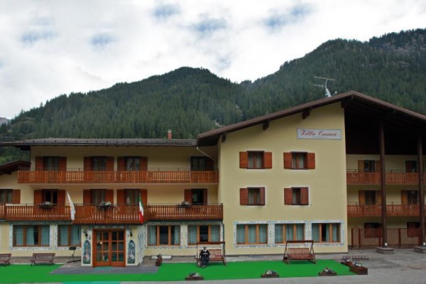 Třípatrová budova hotelu s dřevěnými balkony před lesem a horami.