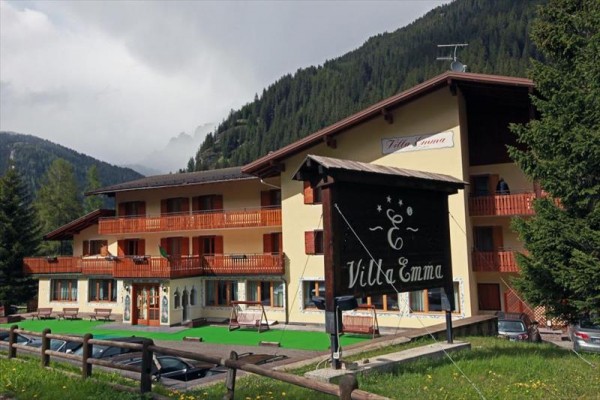 Horský hotel Villa Emma se žlutou fasádou a dřevěnými balkony obklopený lesy.