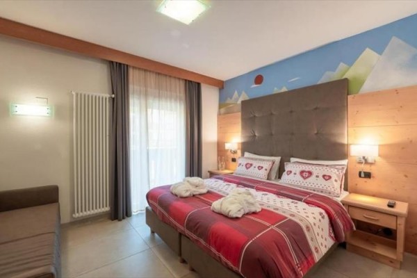 Moderně zařízená hotelová ložnice s velkou postelí a barevným povlečením.