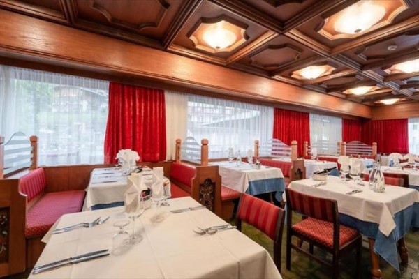 Restaurace s dřevěným stropem a prostřenými stoly s bílými ubrusy a červenými židlemi.