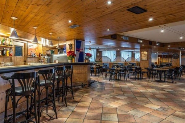 Stylový interiér restaurace s dřevěným obložením, barovým pultem a prázdnými stoly.