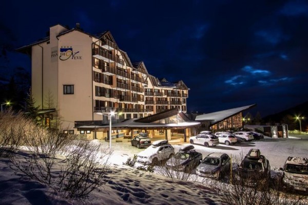 Hotel s osvětleným parkovištěm v zimní krajině při setmění.