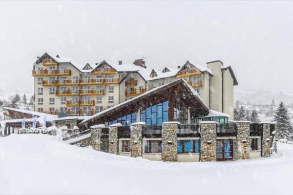 Horský hotel pokrytý sněhem s dřevěnými balkony.