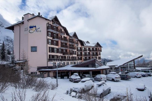 Hotel ve zasněžené krajině s parkovištěm plným aut.