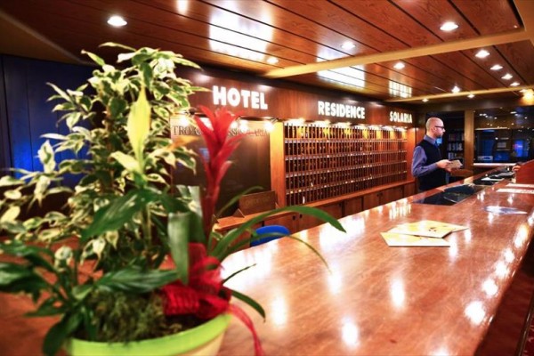 Recepce hotelu s dřevěným pultem a květinou v popředí.
