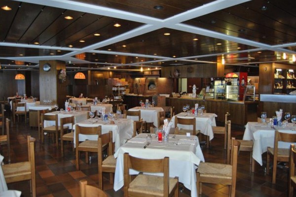 Restaurace se dřevěným nábytkem a prostřenými stoly pod stropem s podhledy.