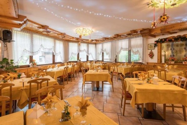 Restaurace s dřevěnými stoly a židlemi, žluté ubrusy a květinová dekorace na stěnách pod okny.