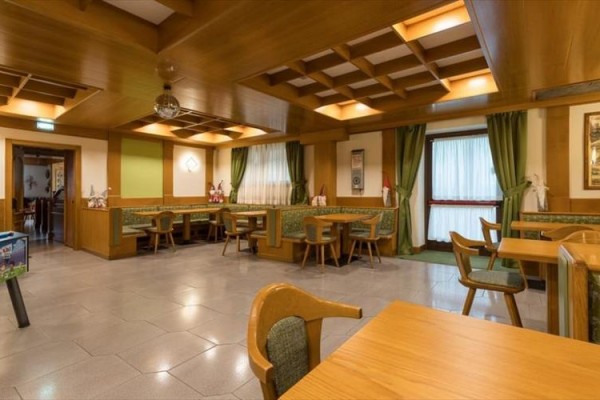 Restaurace s dřevěnými stoly, zelenými závěsy a dekoracemi.