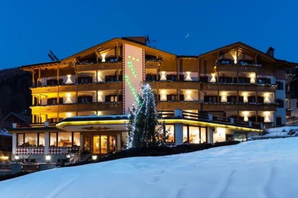 Hotel se světlým dřevěným obložením a osvětlením v zasněžené krajině při soumraku.