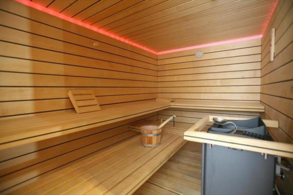 Dřevěná sauna s lavicí a kamny, lemovaná červenými LED světly.