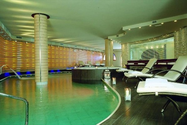 Luxusní interiér wellness s bazénem, lehátky a svíčkami.