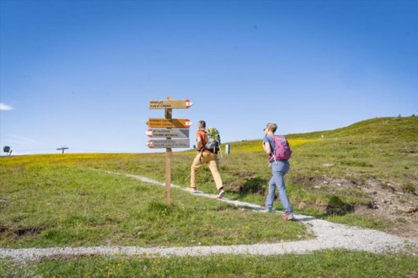 Pár turistů stoupá po pěšině vedle směrového ukazatele na louce.