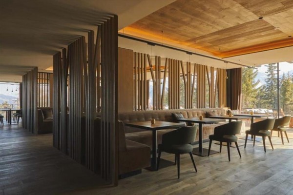 Moderní interiér kavárny s dřevěným designem a velkými okny.