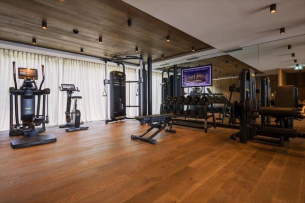 Moderní fitness centrum s různým cvičebním vybavením na dřevěné podlaze.
