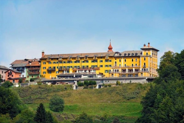 Velká žlutá budova hotelu umístěná na zeleném svahu s modrou oblohou.