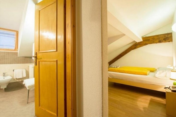 Pohled do ložnice s manželskou postelí a koupelnou s bidetem v podkrovním pokoji.