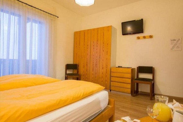 Hotelový pokoj s dvojlůžkem, skříní, televizí a snídaní na stole.