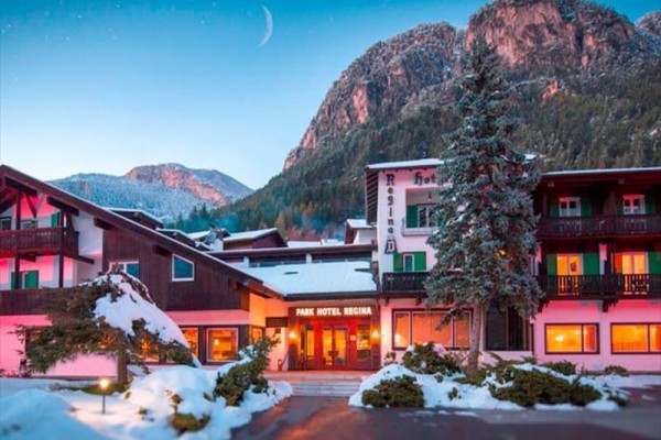 Zimní horský hotel osvětlený v noci s horami v pozadí.