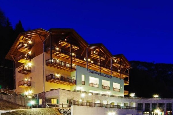 Osvětlený hotel s dřevěnými balkony na horském svahu za soumraku.