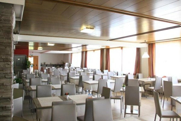 Prostorná restaurace s mnoha stoly a šedými židlemi.
