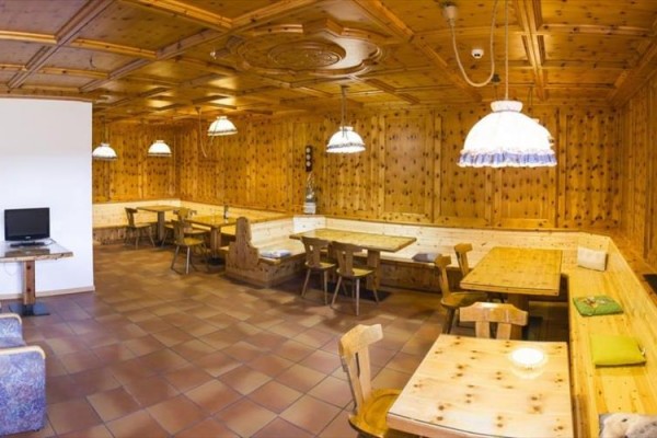 Dřevěná jídelna s několika stoly a židlemi, osvětlená závěsnými lampami.