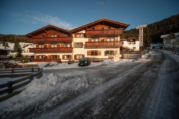 Zasněžená silnice vede k horskému hotelu s dřevěnými balkony.