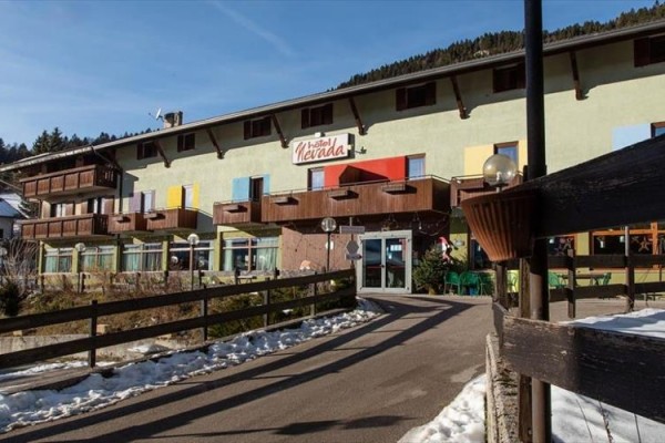 Hotel s dřevěnými balkóny a nápisem na fasádě v horské oblasti.