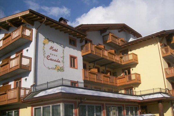 Hotel s dřevěnými balkony a malbou květin na stěně pod modrou oblohou.