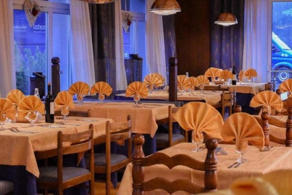 Elegantně prostřená restaurace s dřevěnými stoly a židlemi a složenými oranžovými ubrousky.  