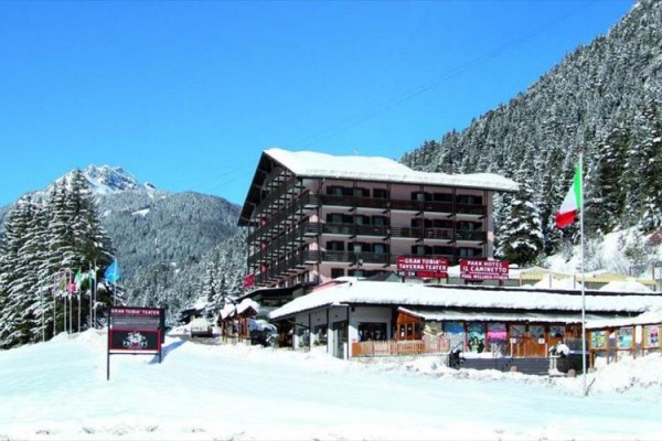 Hotel ve zasněžené horské krajině s italskou vlajkou v popředí.
