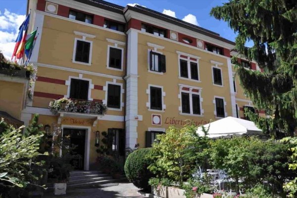 Budova hotelu s žlutou fasádou a rozkvetlou zahradou vpředu.