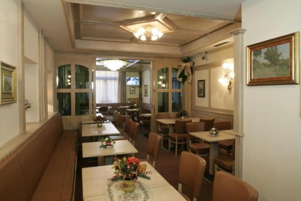 Interiér restaurace s dřevěnými stoly a židlemi, ozdobený květinami.