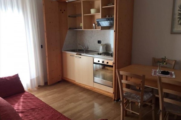 Malá kuchyňská linka s dřevěnými skříňkami vedle jídelního stolu a pohovky.  