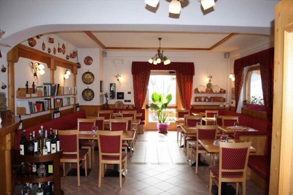 Interiér restaurace s dřevěným nábytkem, knihami na policích a velkou rostlinou uprostřed.