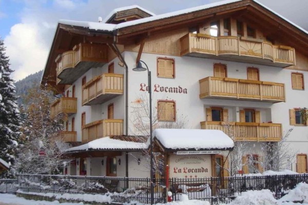 Dvoupatrová horská chata La Locanda s dřevěnými balkony pokrytá sněhem.