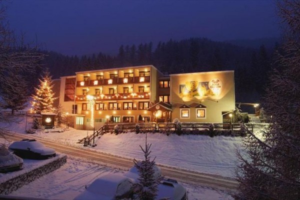 Zasněžený hotel osvětlený v noci s vánočním stromkem vedle budovy.  