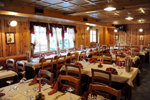 Restaurace s dřevěným obložením a prostřenými stoly s bílými ubrusy a vínovými ubrousky.