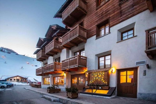 Hotel s dřevěnými balkony u zasněženého svahu v podvečer.
