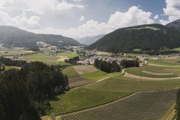 Panoramatický pohled na vesnici uprostřed zelených polí a kopců s lesy.