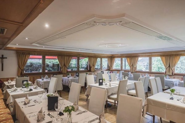 Elegantní restaurace s bílými ubrusy a velkými okny s výhledem do přírody.