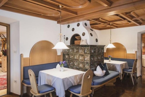 Restaurace s dřevěným obložením a tradiční kachlovou kamnou uprostřed místnosti.