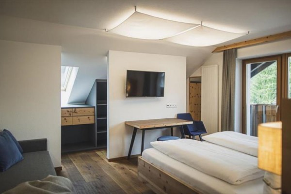 Moderní hotelový pokoj s dvojlůžkem, pracovním stolem, televizí a balkonem.