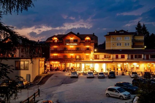 Hotel osvětlený za soumraku s několika auty zaparkovanými před ním.  